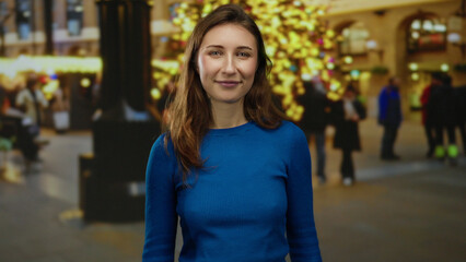 Woman smiling on city street during holiday night with bright lights and festive ambiance, young woman in blue sweater enjoying vibrant urban atmosphere outdoors.