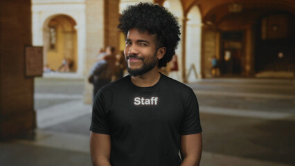African american man in staff uniform smiling outdoors with arched building background.