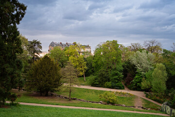 Spring blossom tree by the lake in Parc des Buttes-Chaumont, Paris, France, with rock cliff and cave entrance in the background on a cloudy spring day
