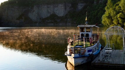 Fototapeta premium A pleasure boat at the pier. A summer morning. A river. The walls of the canyon are reflected in the water.
