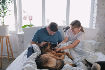 happy millennial couple having breakfast in bed and enjoying fun time with their dogs