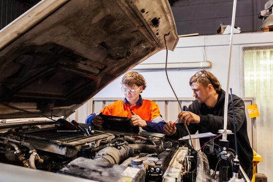 Aussie workman using digital diagnostics tool working on car vehicle engine in mechanics workshop