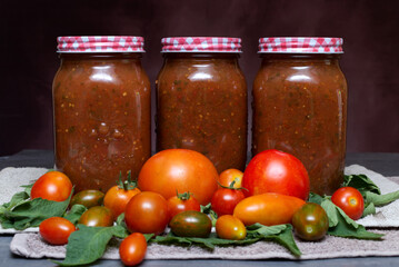 Jars of Tomato Sauce with Fresh Tomatoes and Basil on a Rustic Background