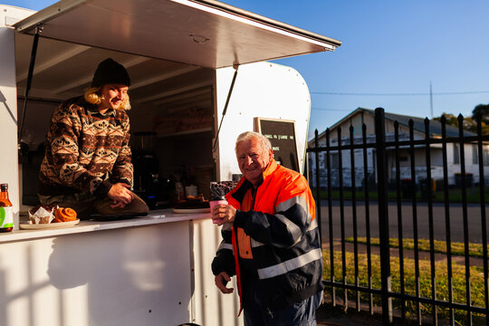 happy older Aussie workman in high vis workwear buying warm takeaway coffee from van