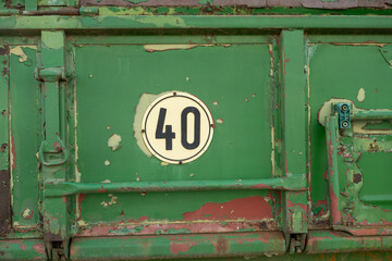 A green, older tractor trailer in a field. The trailer has a round sticker with a number 40 on it.
