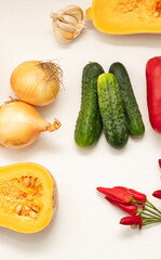 Top view of freshly picked onions, cucumbers, garlic, chili peppers, and butternut squash arranged on a white surface. Concept of farm-to-table freshness and eco-friendly nutrition
