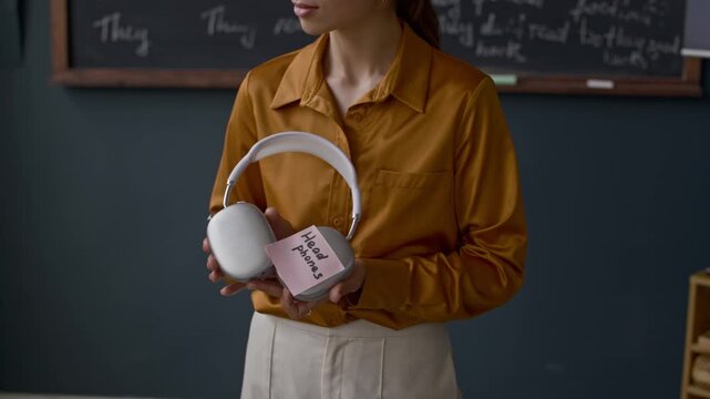 Cropped shot of Muslim student and female teacher labelling classroom objects like pencil case and headphones with sticky notes to practice new words during interactive English lesson
