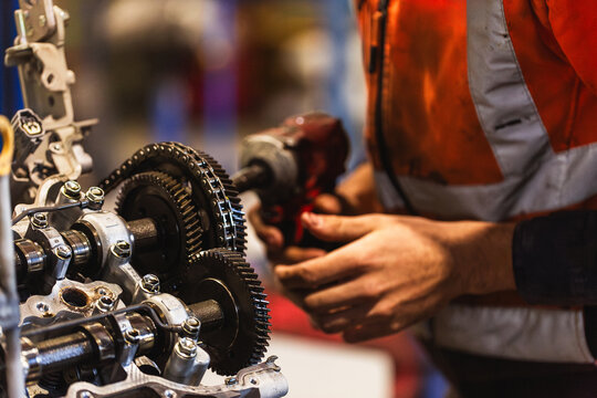Hand of a mechanic using a drill tool to pull apart and repair car engine inside industrial workshop