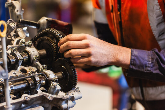 Hand of a mechanic using a drill tool to pull apart and repair car engine inside industrial workshop