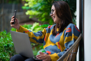 A young Asian woman wearing a yellow floral-pattern sweater and sunglasses, smiling brightly while...
