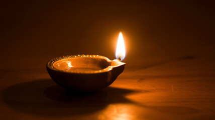 Close-up shot of a diya lamp, made of clay, filled with oil and a cotton wick, lit, casting a warm glow, soft diffused lighting, chiaroscuro, monochromatic scheme, smooth texture, on a wooden surface.