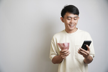 A smiling man holds banknotes and a smartphone with a happy and satisfied expression, symbolizing a financial gain.