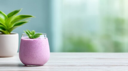 A refreshing pink smoothie topped with mint leaves, placed beside a small green plant on a wooden table, evoking a tranquil and healthy lifestyle.