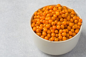 Bowl filled with sea buckthorn berries on a gray background, horizontal, close up. Concept of healthy eating, vitamins.