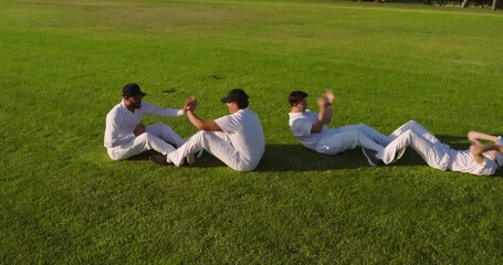 Central duo initiating sit-up clap wave, Diverse male teammates strengthening core on grass field