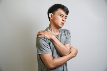 Obraz premium A man shows pain in his shoulder with a pained expression, indicating muscle strain or injury, while clenching his fist.
