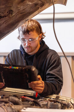 Aussie workman using digital diagnostics tool working on car vehicle engine in mechanics workshop