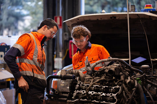 Two male mechanics inspecting vehicles engine in workshop - Powered by Adobe