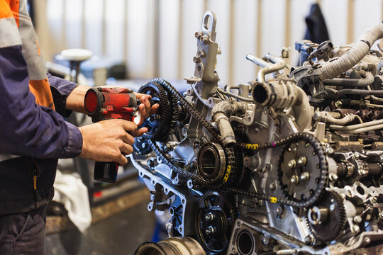 Hand of a mechanic using a drill tool to pull apart and repair car engine inside industrial workshop