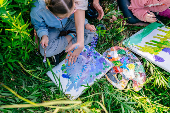 Child stamping lupine shapes on canvas with teacher guidance during a nature-inspired art lesson