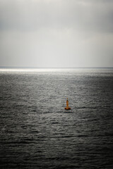 orange buoy in the open, calm, dark sea with rays of light in the background - after storm mood