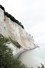 coast with bright high stone cliff with isolated greenery on it at the light blue water