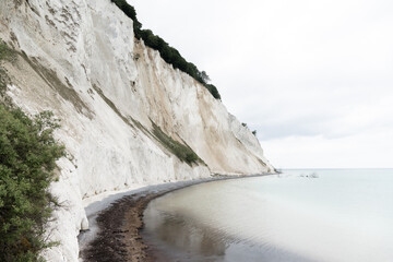 coast with bright high stone cliff with isolated greenery on it at the light blue water