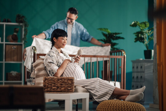 Pregnant woman holding baby shoes while man making crib in baby room - Powered by Adobe