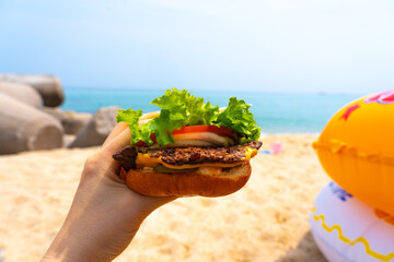 Woman holding burger in a hand against beach background