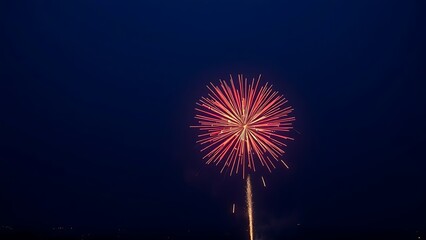 Single firework bursting in red and gold against twilight sky, radiant sparks trailing over distant city lights.
