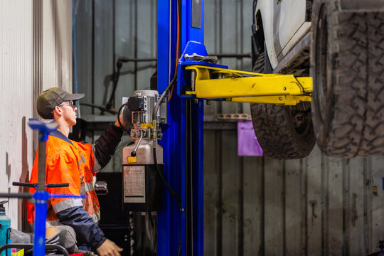 young man mechanic worker working car lift in workshop to fix mining fleet vehicle