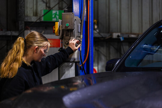 Long-haired mechanic operating a control panel of blue hydraulic lift system