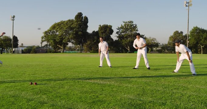 Lobbing ball in air, diverse male teammates catching in park practicing before batsman holding bat