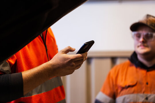 Aussie mechanic holding a mobile phone inside industrial workshop
