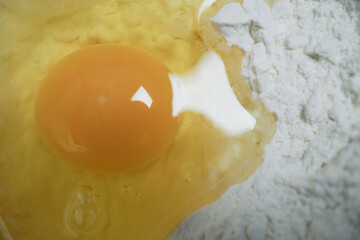 Close up of raw egg with bright yellow yolk sits next to pile of white flour, ready for baking. image captures smooth texture of yolk and powdery surface of flour