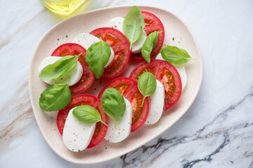 Beige plate with italian classic caprese salad on a white granite background, horizontal shot, high angle view