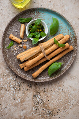 Plate with grissini breadsticks and basil oil on a beige granite background, vertical shot, top view