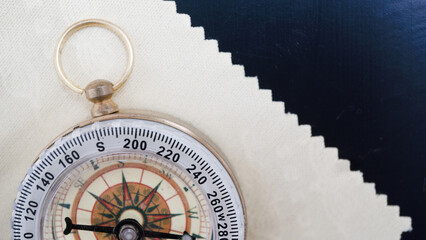 Vintage compass with brass ring rests on textured surface, partially covered by piece of fabric. compass needle points north, evoking sense of adventure and exploration
