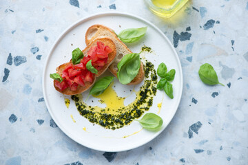 Plate with tomato bruschettas and basil oil, horizontal shot on a white and blue granite background, above view