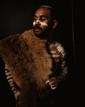 Aboriginal man wearing a fur cloak standing in dark background