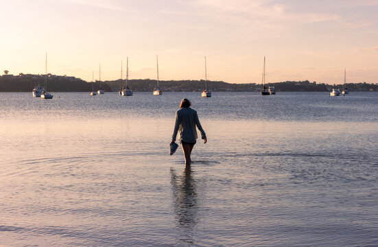 Young teenage girl standing in calm water in the late afternoon with boats in the background