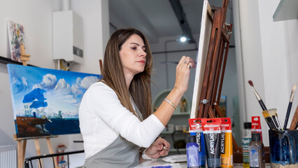 In an art studio, a beautiful middle-aged woman is happily working on a painting on an easel