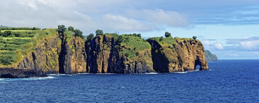 Coastal cliffs looking like a giant elephant with vegetation at the edge of the blue ocean and cloudy sky, Miradouro da Tromba de Elefante, Capelas, Sao Miguel Island, Azores, Portugal