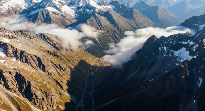 Aerial view of rugged mountain range with snow-capped peaks and low-hanging clouds at sunrise