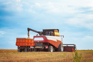 Obraz premium Industrial combine harvester unloading grains into trailer in agricultural field on summer day in countryside