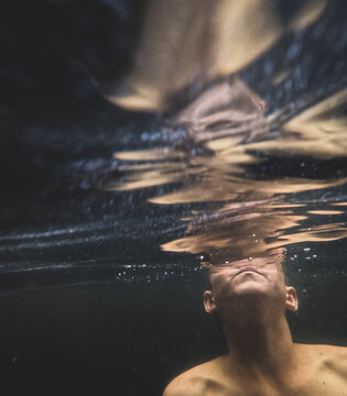 Boy submerged under clear water with shoulders and lower face visible blowing bubbles to surface