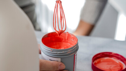 A close-up shot of pink paint being stirred and prepared with a mixing brush in its container at an...