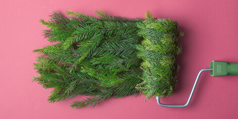Paint roller wrapped in spruce rolls festive green texture on pink background, witty Christmas DIY concept for winter promotions.