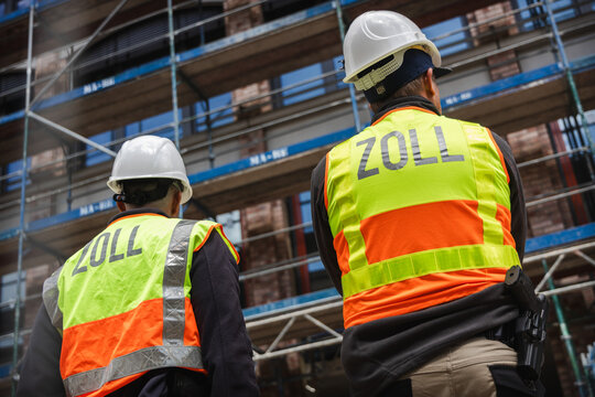 Beamte bewachen eine Baustelle und tragen einen Schutzhelm sowie gelbe Warnwesten