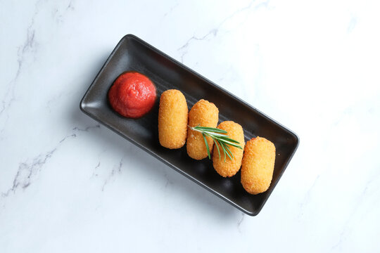 Four golden-brown fried croquettes with red sauce on the side topped with a herb